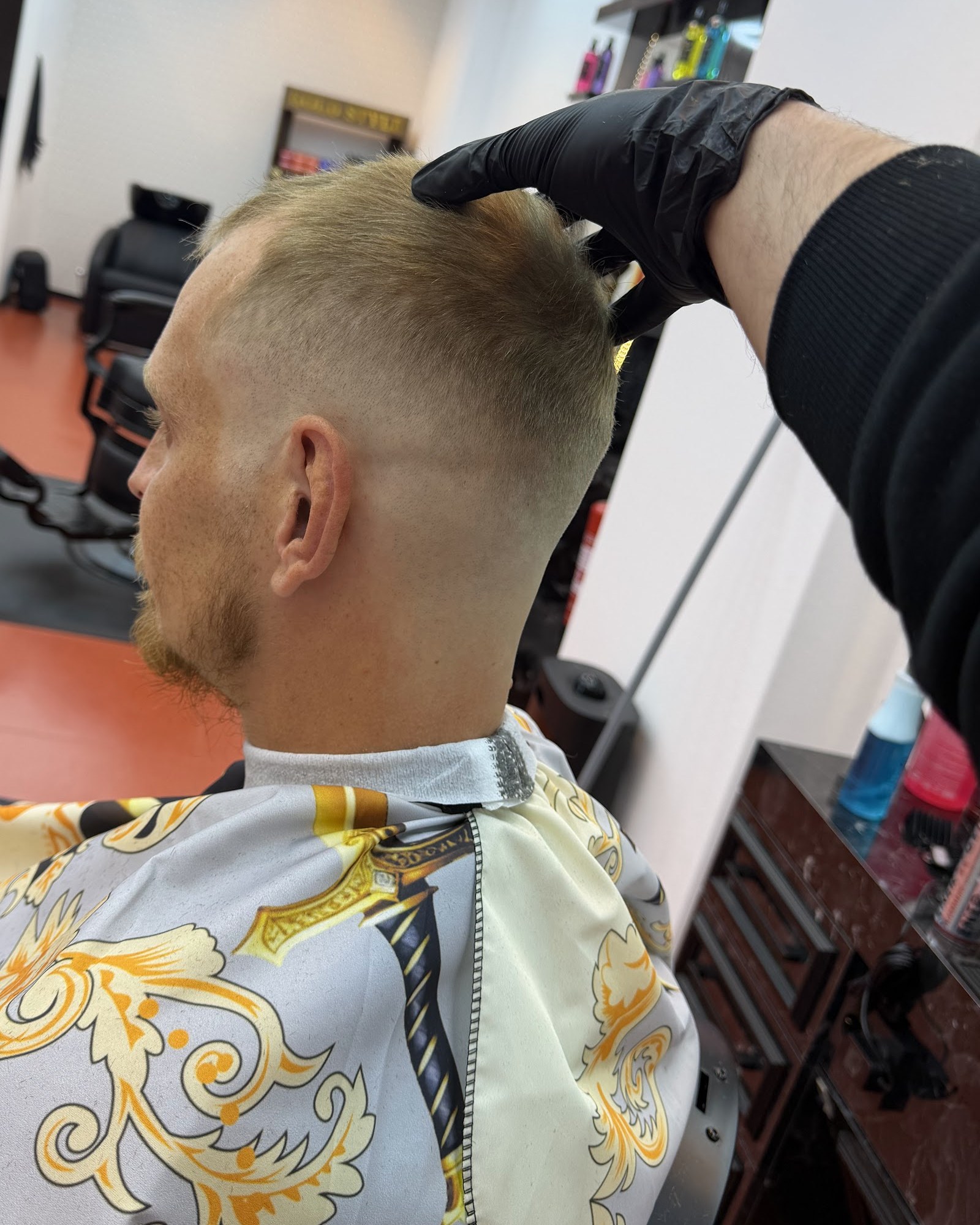 Een verse skin fade, van achteren gezien, met een gouden kapmantel om