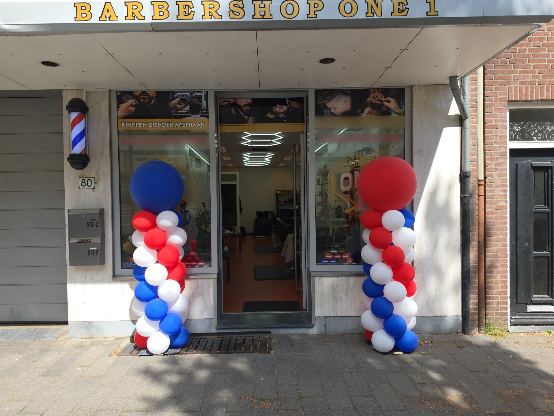 De winkelpui van Barbershop One aan de Akerstraat 80, met gouden letters boven de deur en een barberpaal
